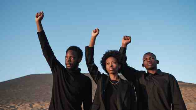 três pessoas negras fazendo sinal de resistência com as mãos levantadas e o punho fechado